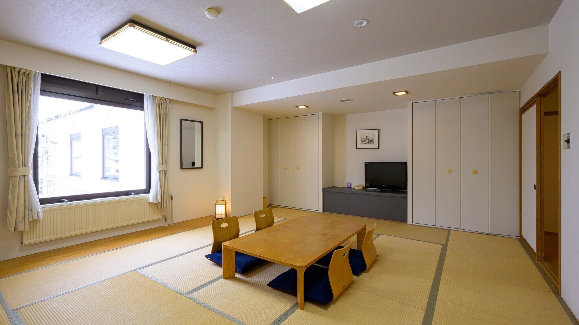A room with tatami mats, a wooden table, a television, and a wardrobe.