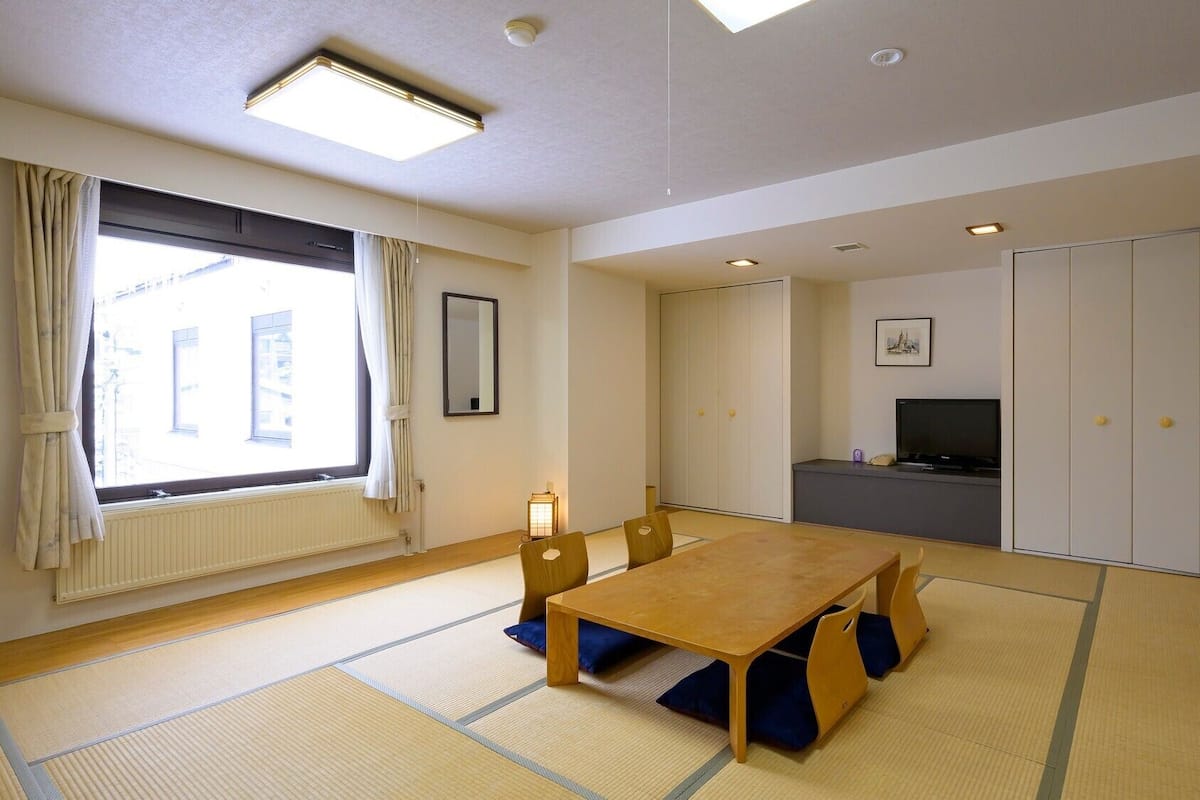 Une pièce avec des tatamis, une table en bois, un téléviseur et une armoire.