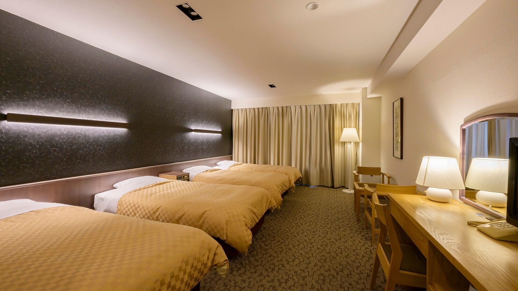 A hotel room with three beds, a desk with a telephone, a lamp, and a mirror.