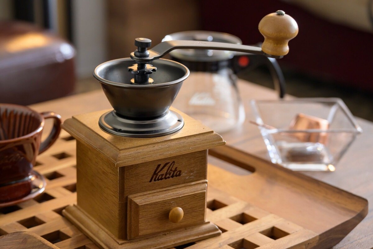Un moulin à café en bois, doté d’une manivelle et posé sur un plateau.