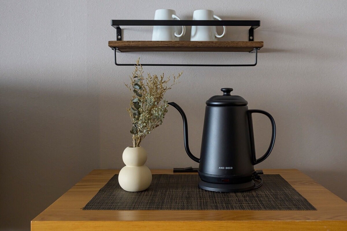 Une machine à café est posée sur une table, à côté d’un vase rempli de fleurs séchées et d’une étagère où sont rangées des tasses.