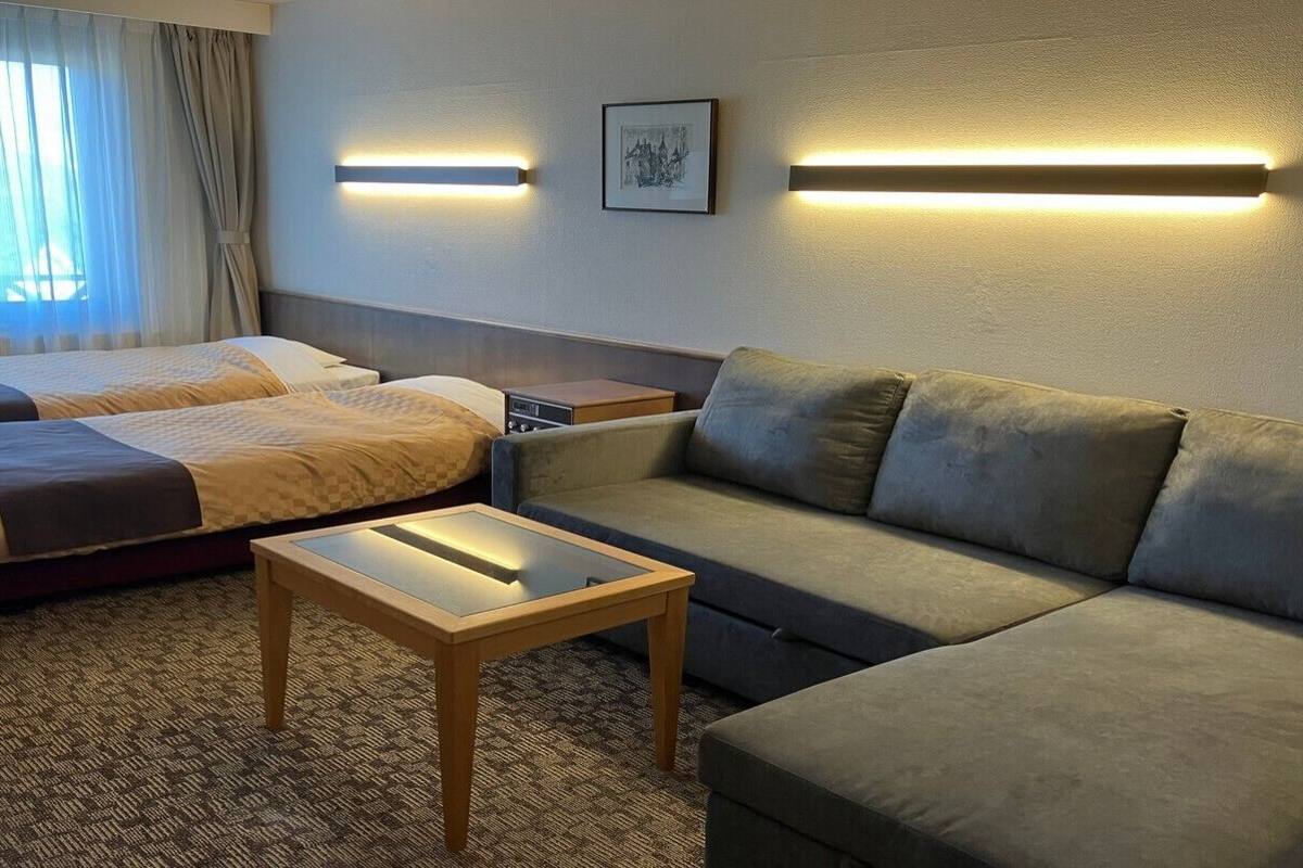 Une chambre d’hôtel avec deux lits, un canapé, une petite table et des lampes fixées au mur.