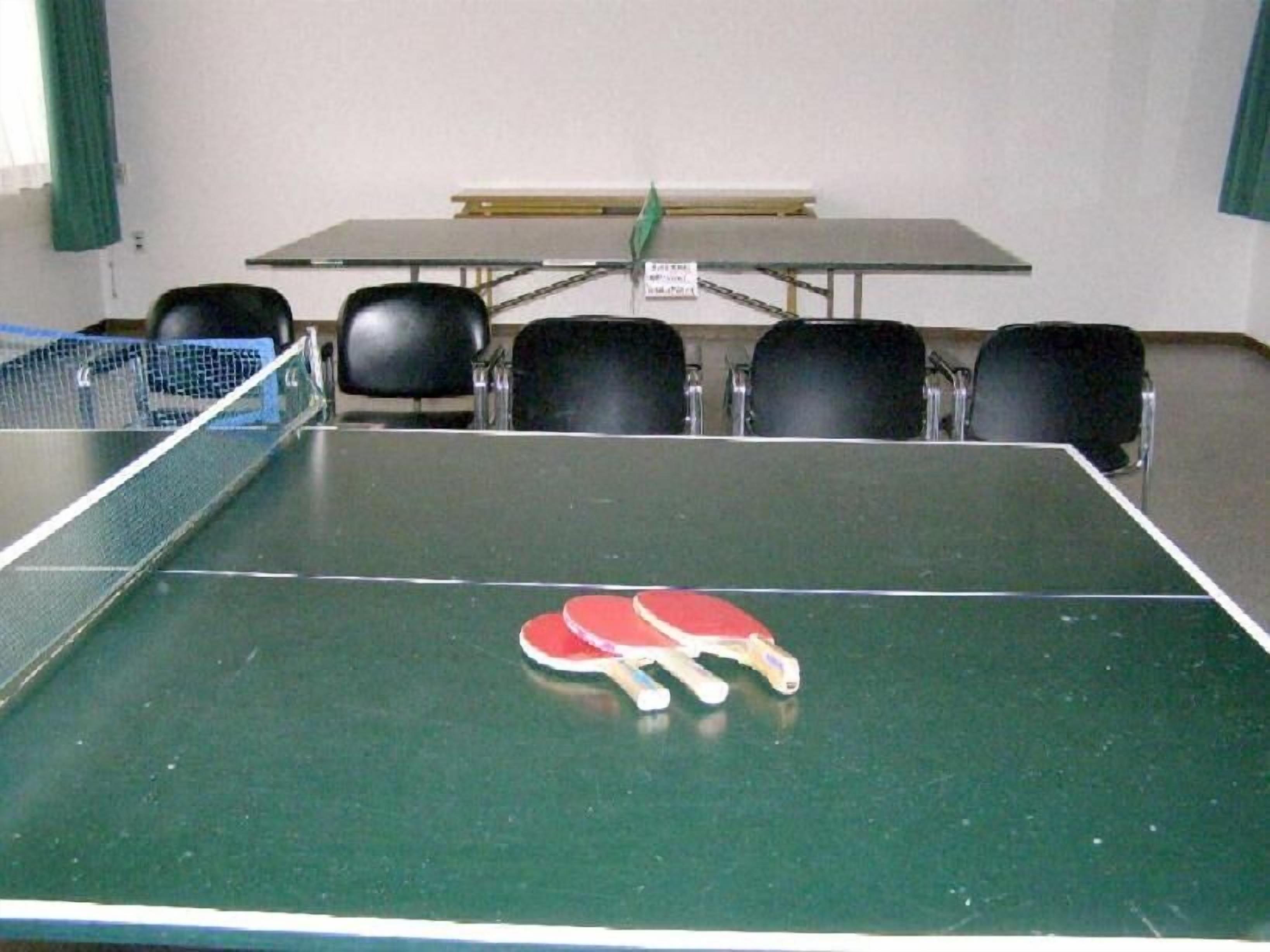 Una mesa de tenis de mesa con cuatro sillas a su alrededor, una paleta de tenis de mesa y una red.