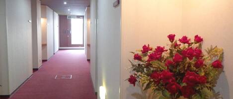 A hotel hallway with a red carpet, a wooden reception desk, and a vase of red flowers on the wall.