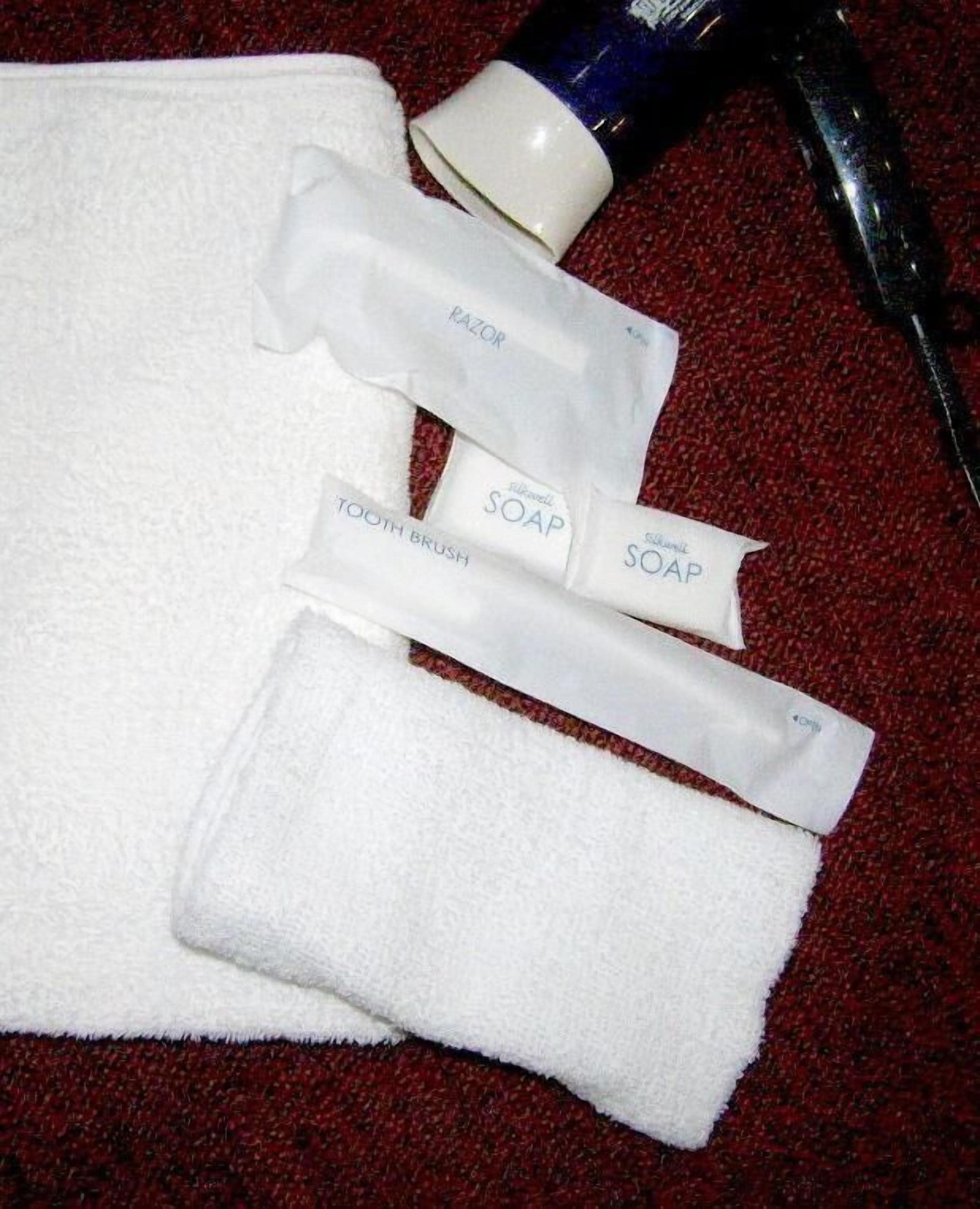 Una toalla blanca, dos pastillas de jabón y un tubo de pasta de dientes sobre una alfombra roja.