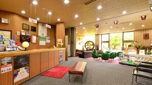 A reception area with a wooden counter, framed certificates, and a seating area with green chairs. - Hotel Masyu (Teshikaga)