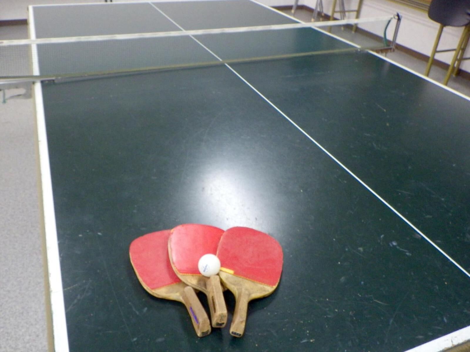 A table tennis table with two red paddles and a white ball.