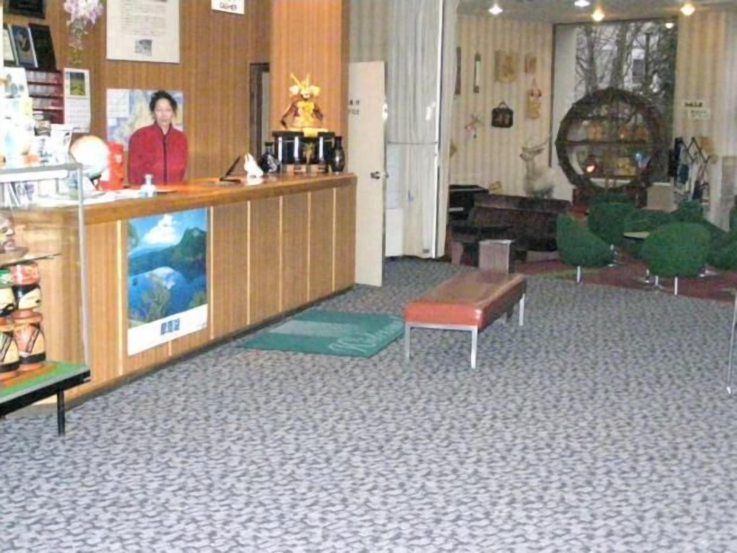 A reception area with a wooden counter, a seated receptionist, a large poster, and a seating area with a bench and green chairs.