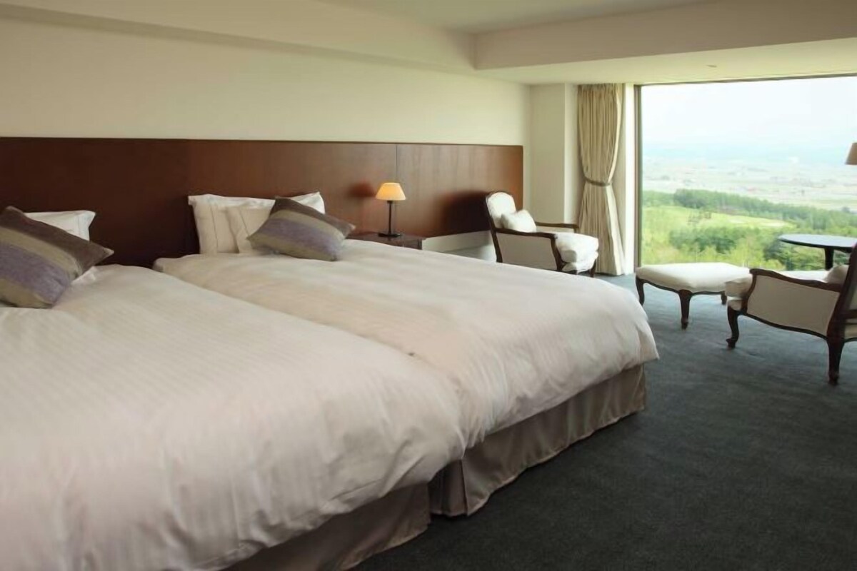 A hotel room with two beds, a desk, and a view of the countryside.