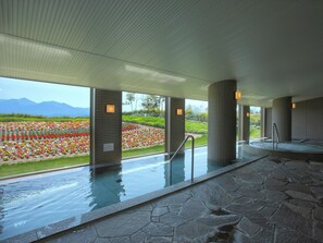 Un área de spa con piscina de piedra, ventanas amplias y vistas a un jardín floral.