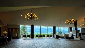 Un hall d’entrée spacieux doté d’un sol en pierre, de grandes fenêtres offrant une vue sur les montagnes et de plusieurs lustres.