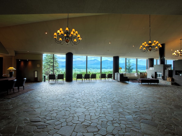 A spacious lobby with a stone floor, large windows offering mountain views, and multiple chandeliers. - Furano Resort Orika (Nakafurano)