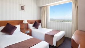 Habitación de hotel con dos camas, una mesita de noche, una lámpara y vista a la ciudad.