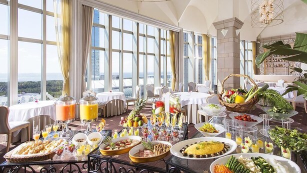 Un buffet de petit-déjeuner proposant une variété d’aliments et de boissons, installé dans une salle dotée de grandes fenêtres et d’un plafond haut.
