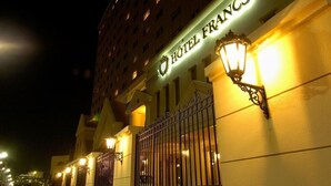 L’entrée d’un hôtel, avec une enseigne indiquant « HÔTEL FRANCS » et une grille fermant l’accès.