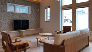 Ein modernes Wohnzimmer mit Fernseher, Holzmöbeln und großen Fenstern.