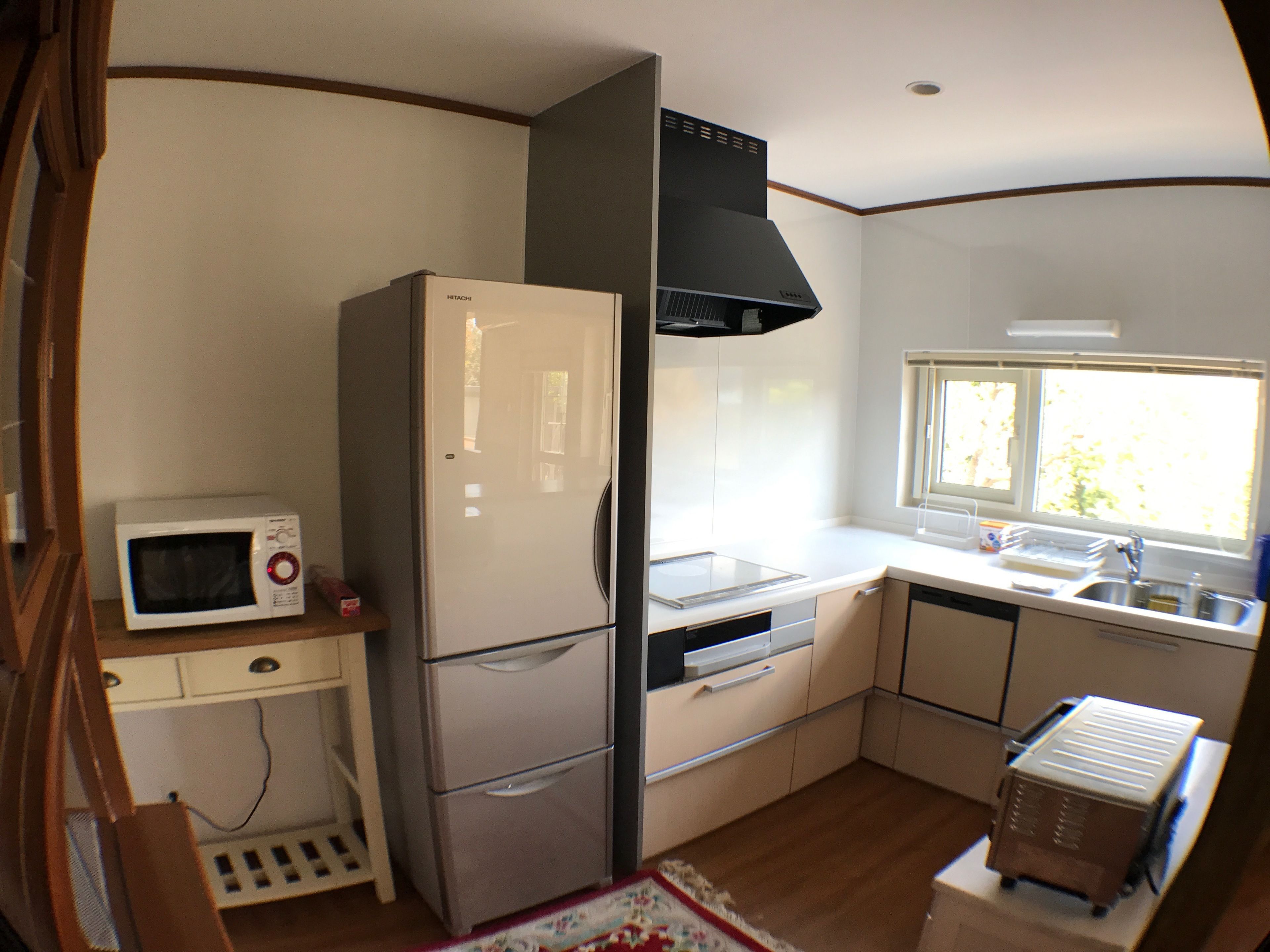 A compact kitchen with a refrigerator, microwave, sink, and a window.