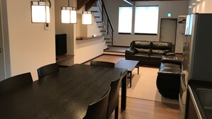 Ein modernes Wohnzimmer mit einer schwarzen Ledersofa, einem Esstisch mit Stühlen und einer Küchenzeile inklusive Kühlschrank und Herd.