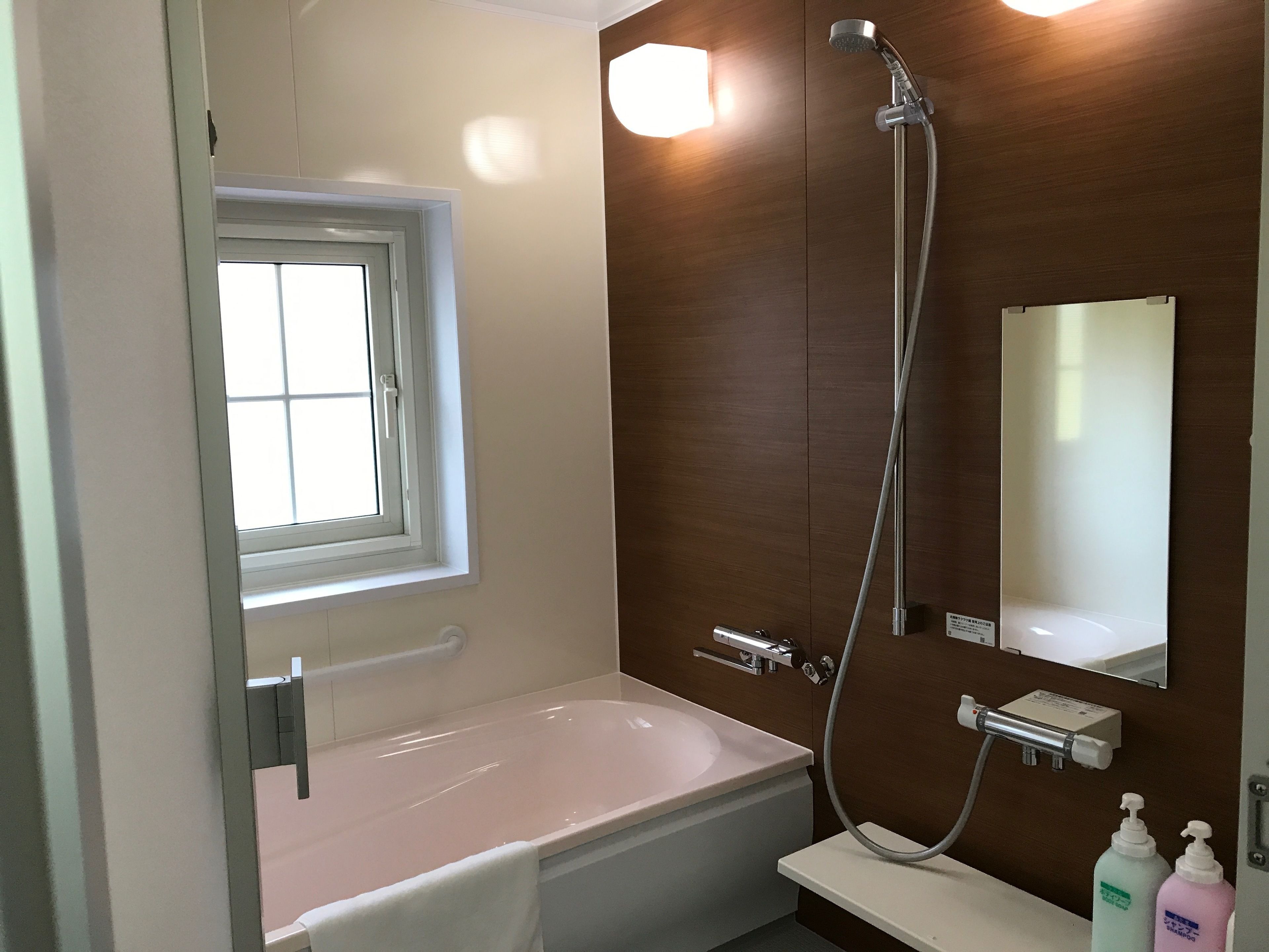A bathroom with a bathtub, a shower, a window, and a mirror.