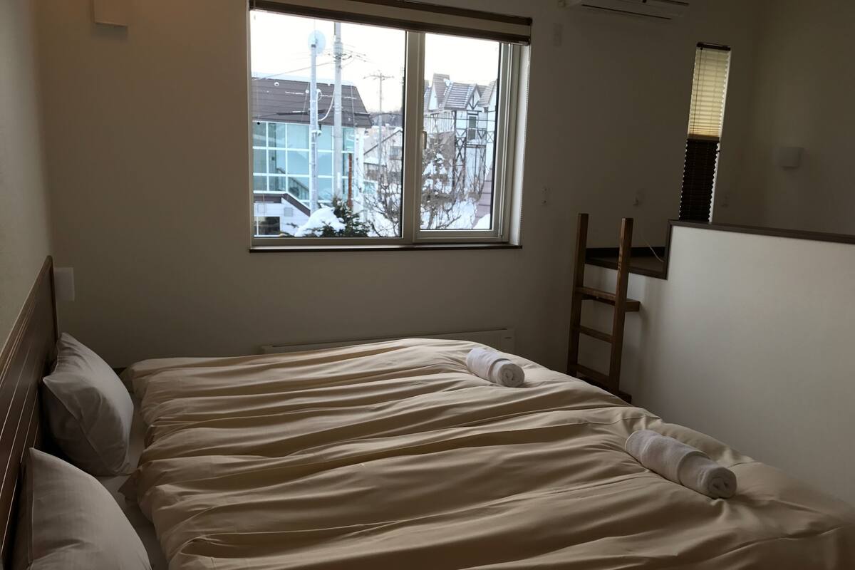 Une chambre avec un grand lit, une fenêtre et une échelle en bois.
