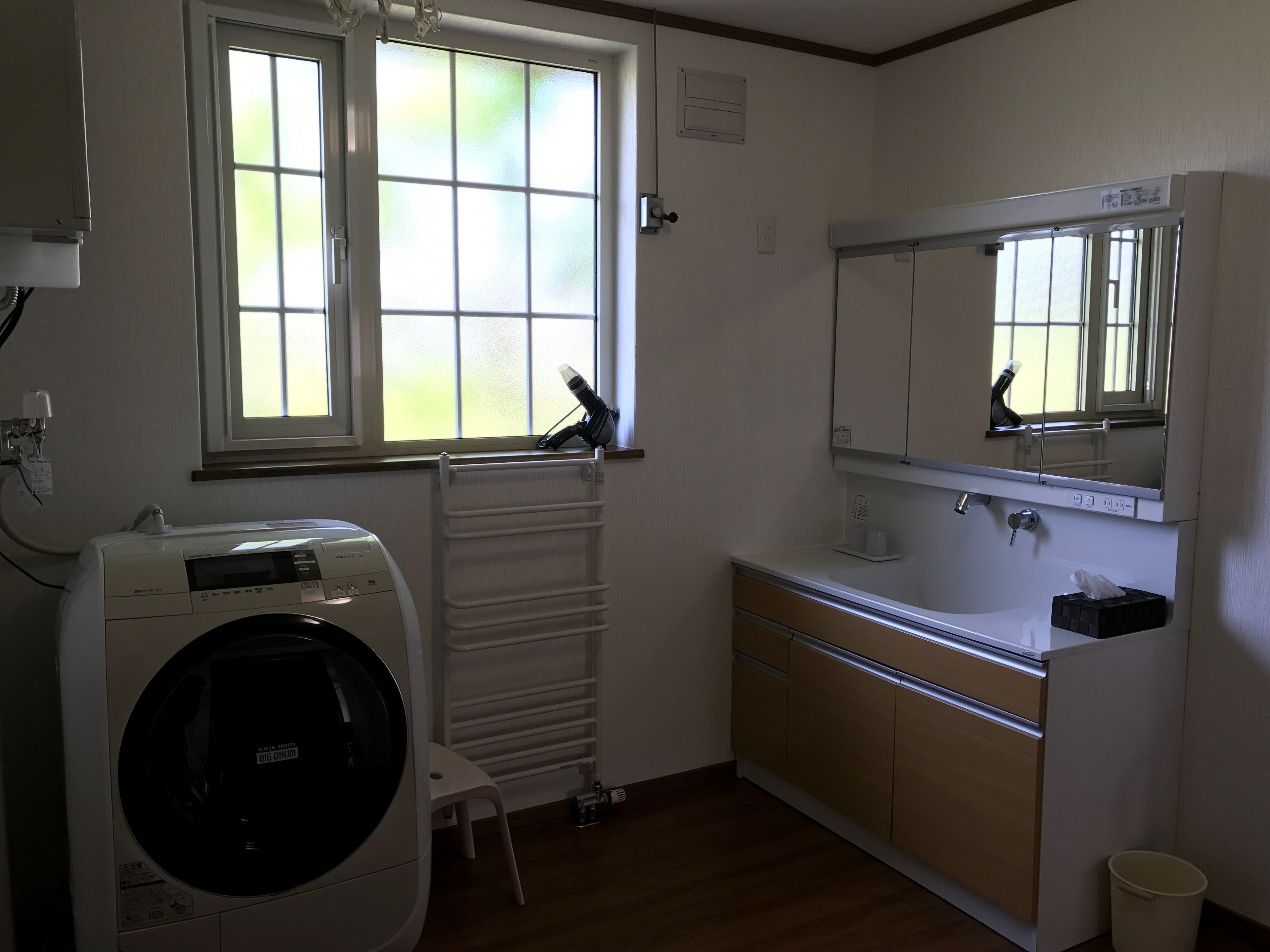 Een compacte, goed verlichte badkamer met een ingebouwde wasmachine, een radiator, een klein krukje en een wastafel met spiegel erboven.