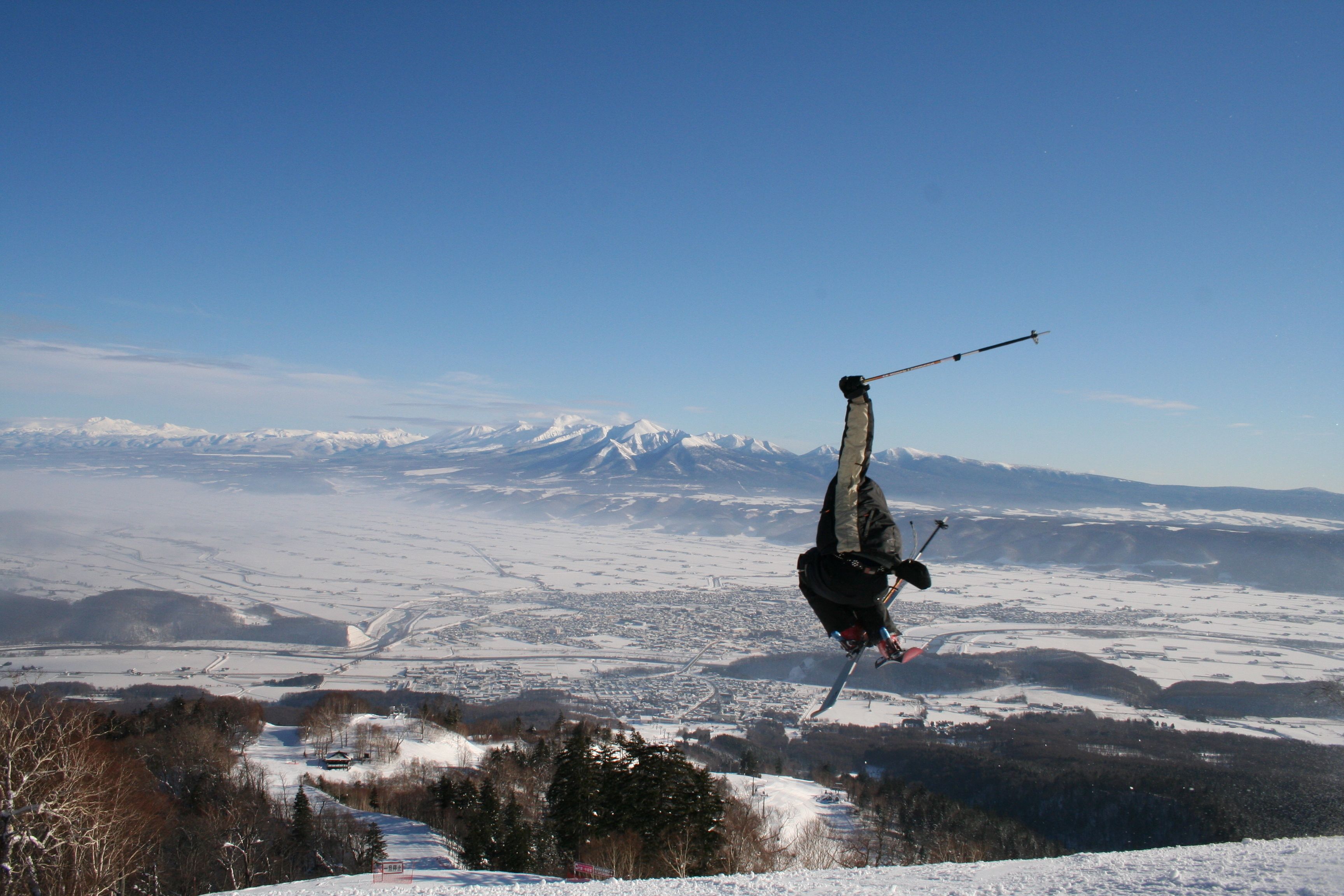 A person skiing on a snowy slope with a clear view of a mountain range and a town in the distance.