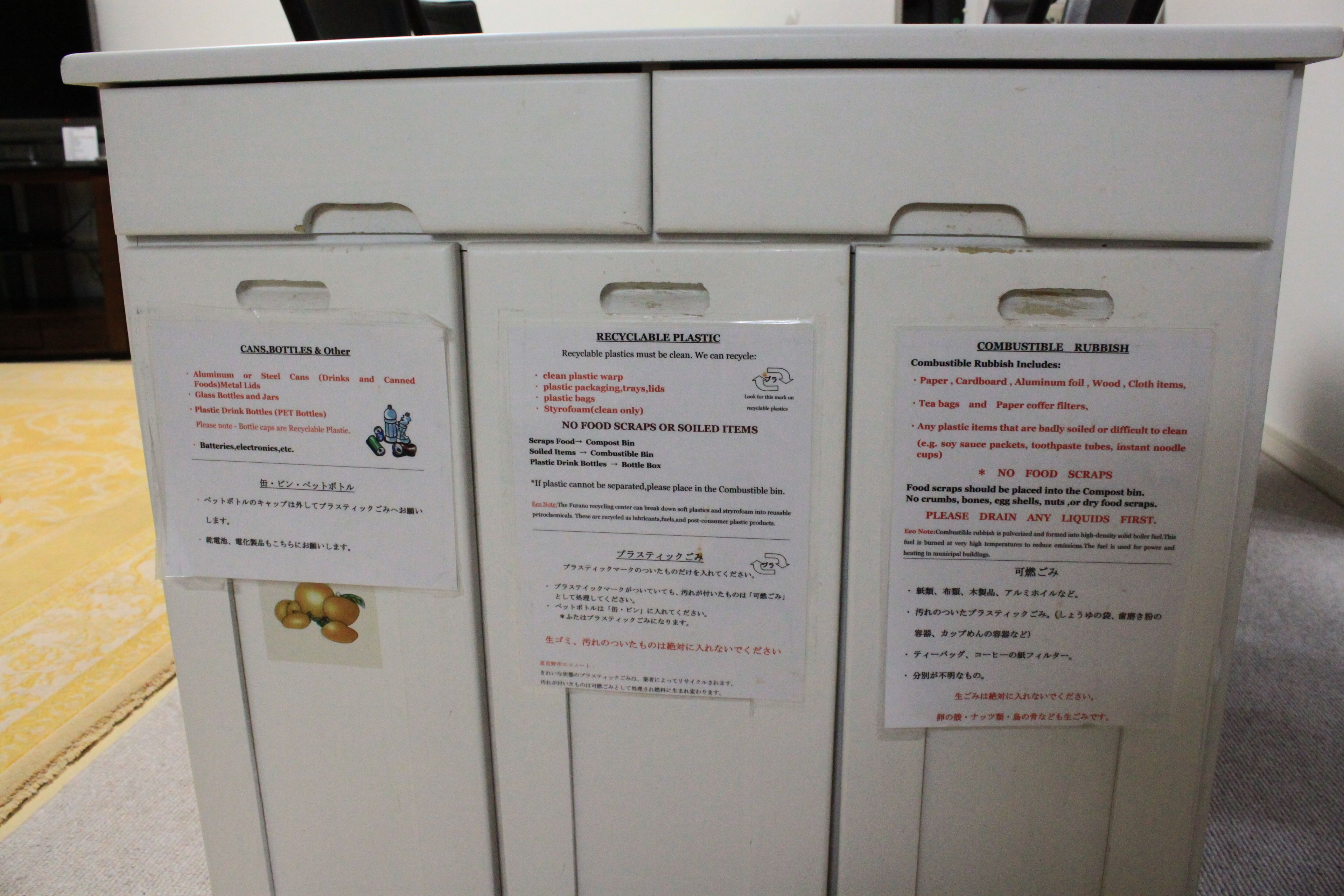 A waste sorting station with labeled bins for cans, bottles, recyclable plastic, and compostable rubbish.