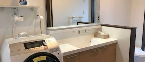 A hotel bathroom with a washing machine, a sink, a mirror, and a trash bin.