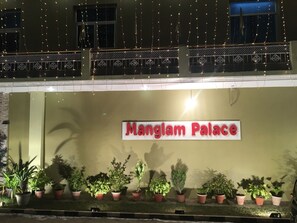 A building with a sign reading 'Manglam Palace' and a balcony with string lights.