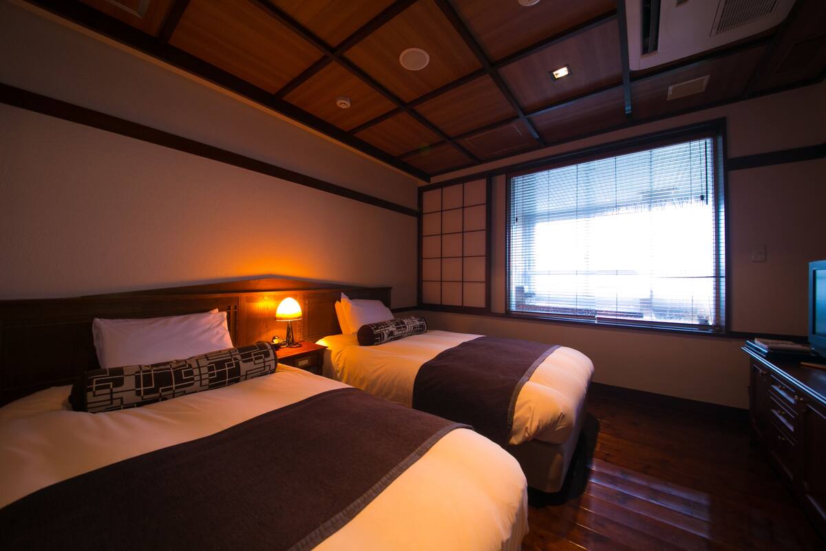 Habitación de hotel con dos camas, techo de madera, ventana con persianas y un televisor sobre un aparador.
