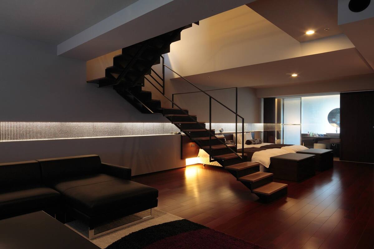 Una sala de estar moderna con una escalera, un sofá, una mesita de centro y una cama.