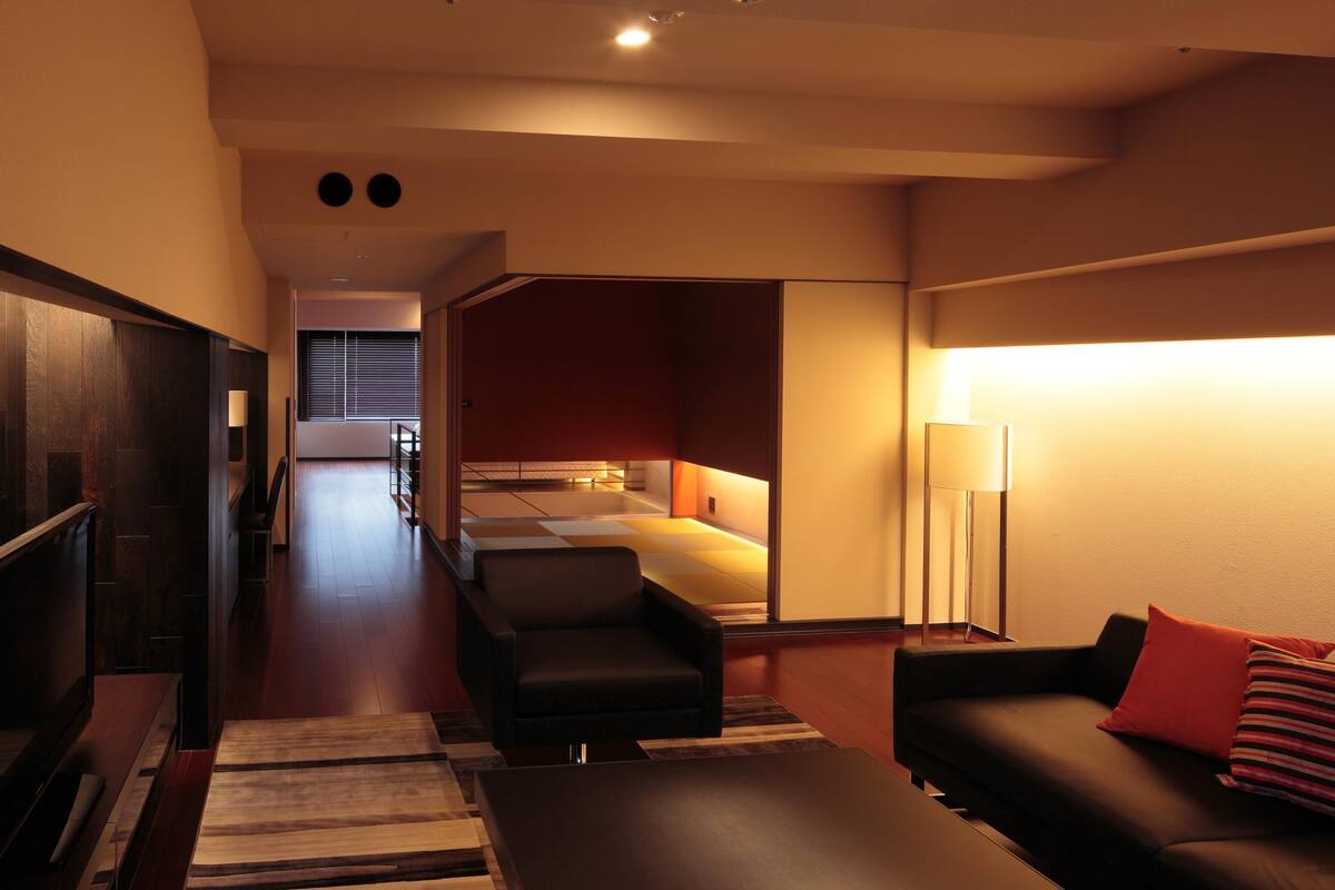 Una sala de estar moderna con un sofá, un sillón y una mesita de centro. Se ve un pasillo que conduce a un dormitorio con un ventanal grande.