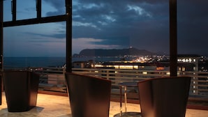 Una terraza con sillas y una mesa, con vistas a un paisaje urbano y al mar al atardecer.