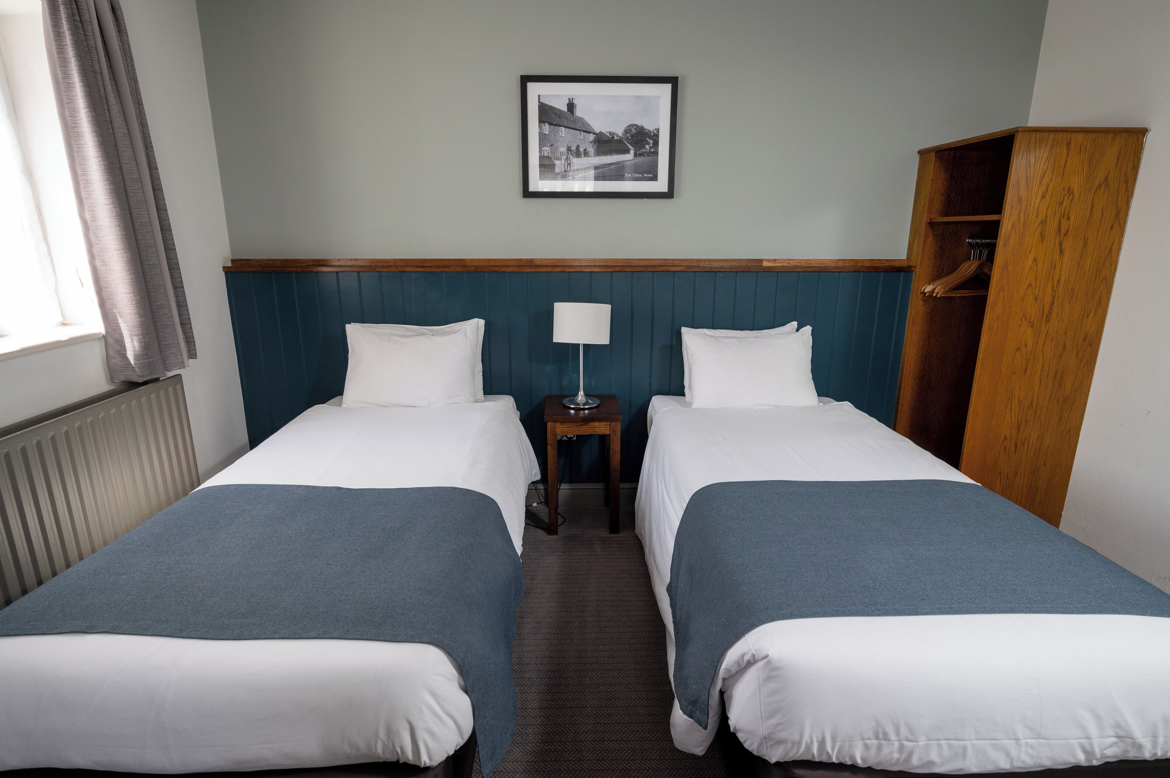 Une chambre d’hôtel avec deux lits, une table de chevet avec une lampe, une armoire en bois et un tableau encadré au mur.