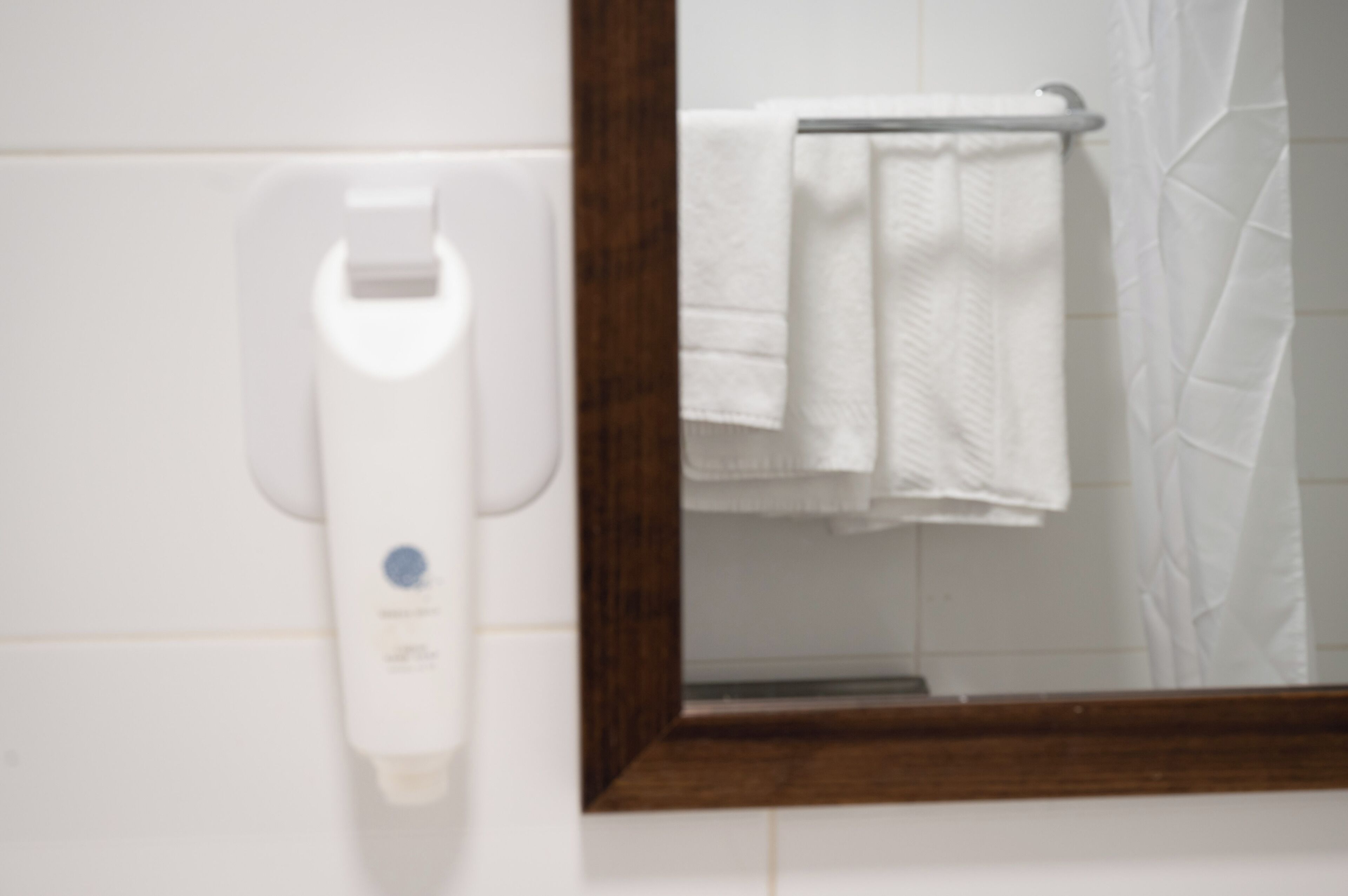A bathroom with a white towel dispenser, a towel rack, and a mirror with a wooden frame.