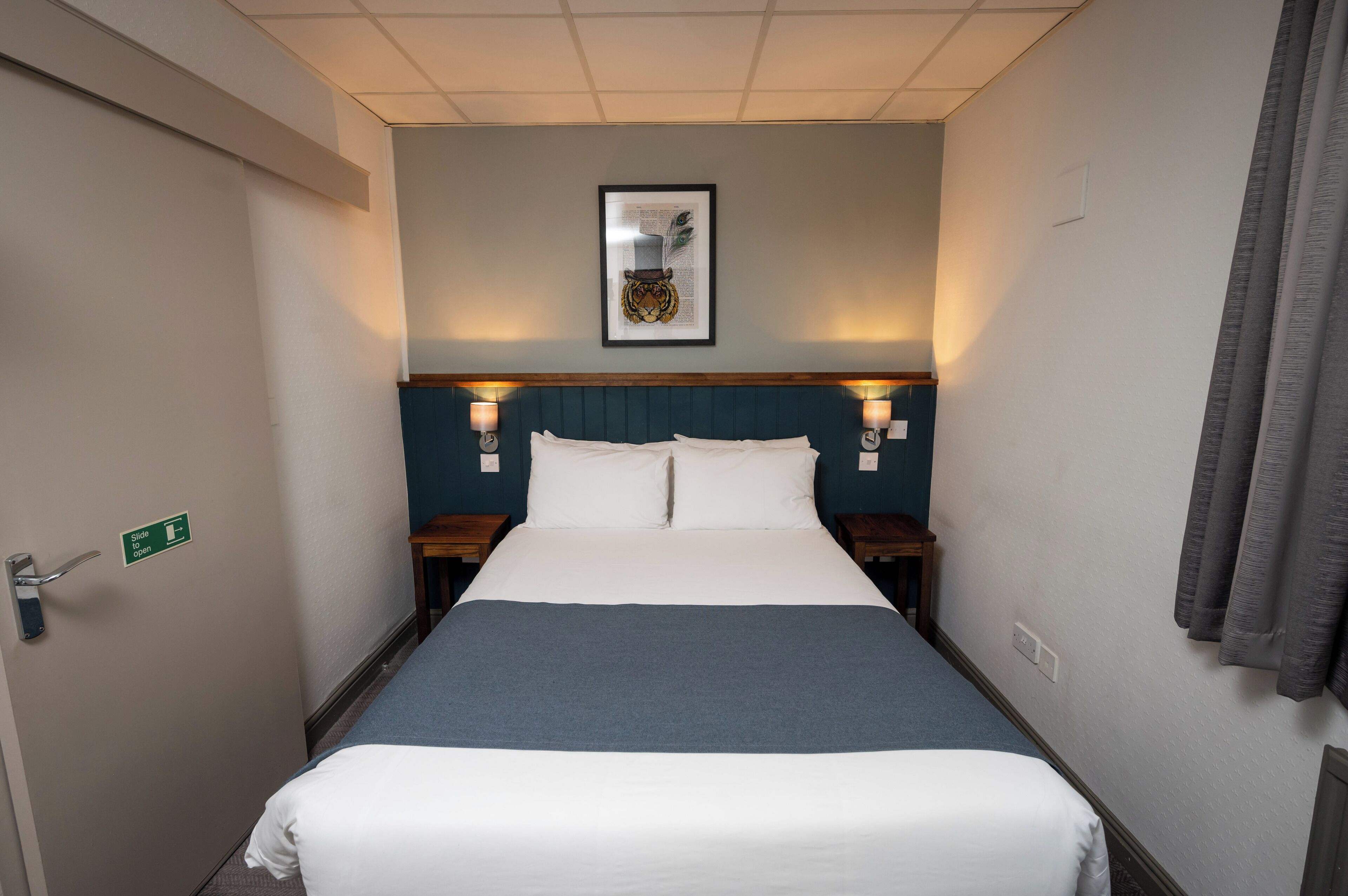A hotel room with a bed, a framed picture on the wall, and a sign indicating the room is open.