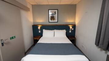 A hotel room with a bed, a framed picture on the wall, and a sign indicating the room is open.