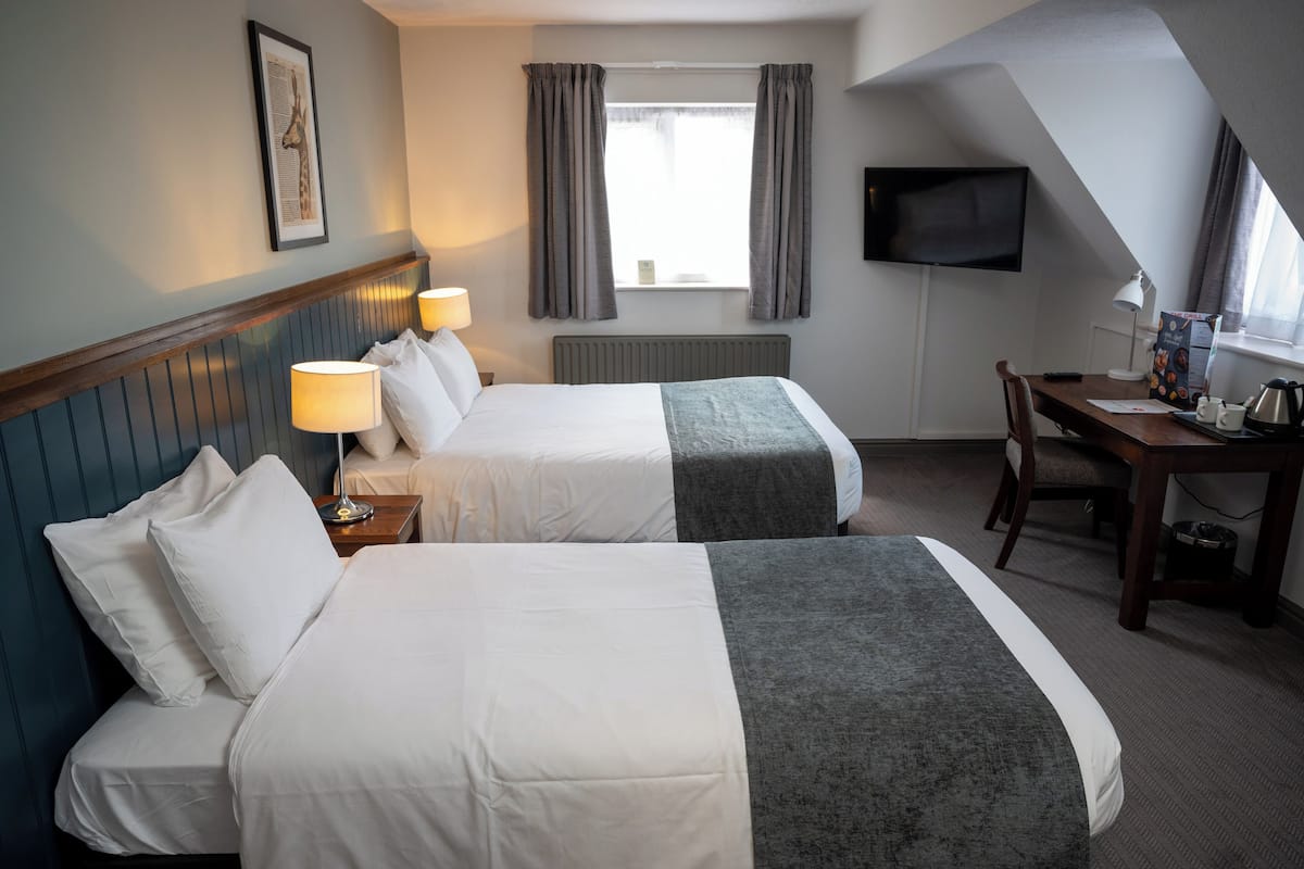A hotel room with two beds, a desk, a chair, a TV, and a window with curtains.