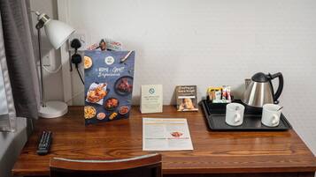 A hotel room desk with a remote control, a menu, a tray with two mugs, a kettle, and a sign indicating no smoking or vaping.