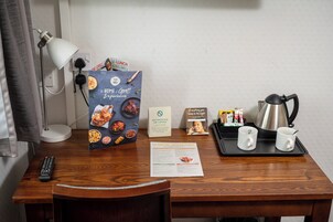 Mesa de quarto de hotel com um controle remoto, um menu, uma bandeja com duas canecas, uma chaleira e uma placa indicando que não é permitido fumar ou usar vaporizadores.