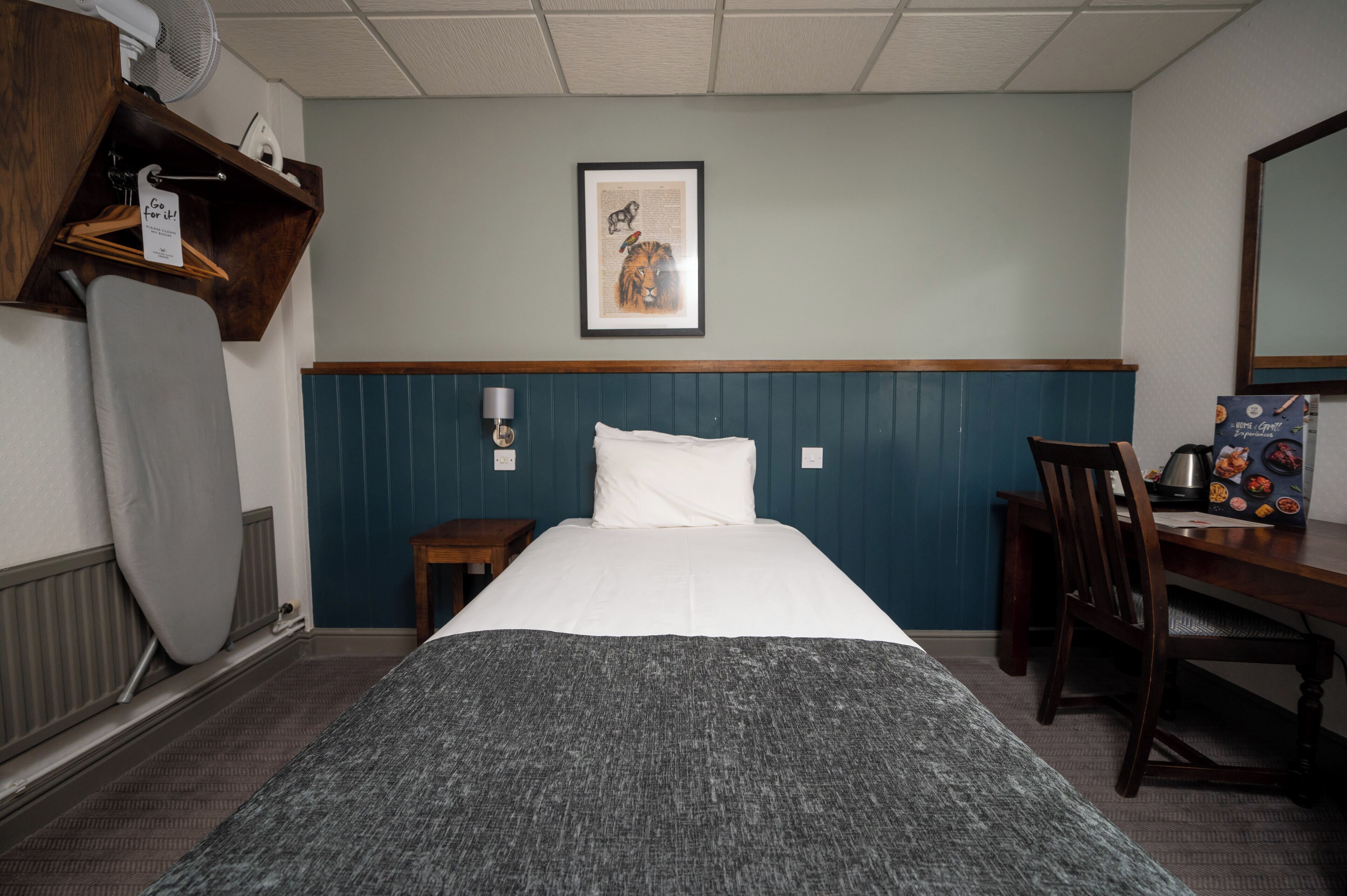 A hotel room with a bed, a desk, a chair, a framed picture on the wall, and a radiator.