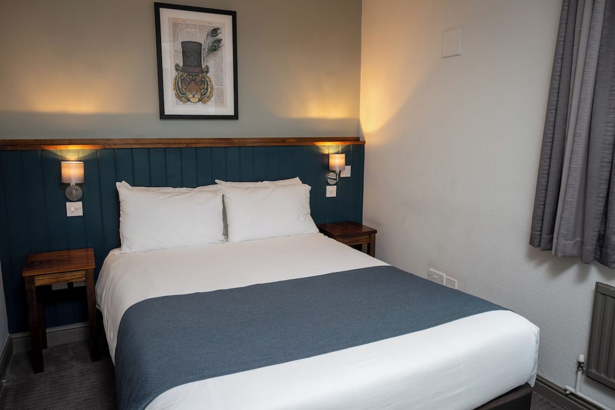 A neatly made bed with a blue blanket, two bedside tables with lamps, and a framed artwork on the wall.
