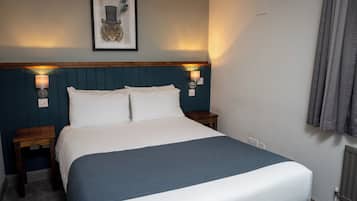 Una cama bien hecha con una manta azul, dos mesitas de noche con lámparas y una obra de arte enmarcada en la pared.