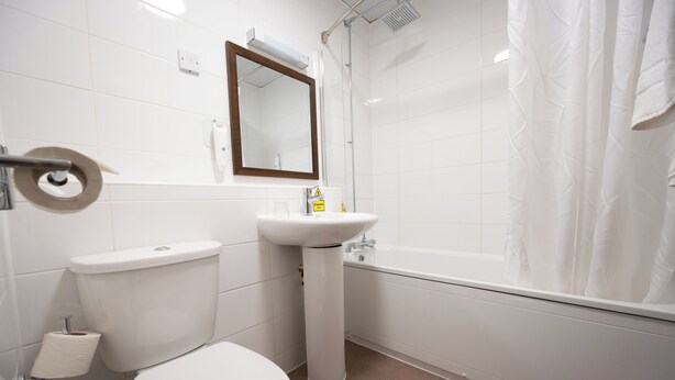A bathroom with a toilet, sink, mirror, and shower curtain.
