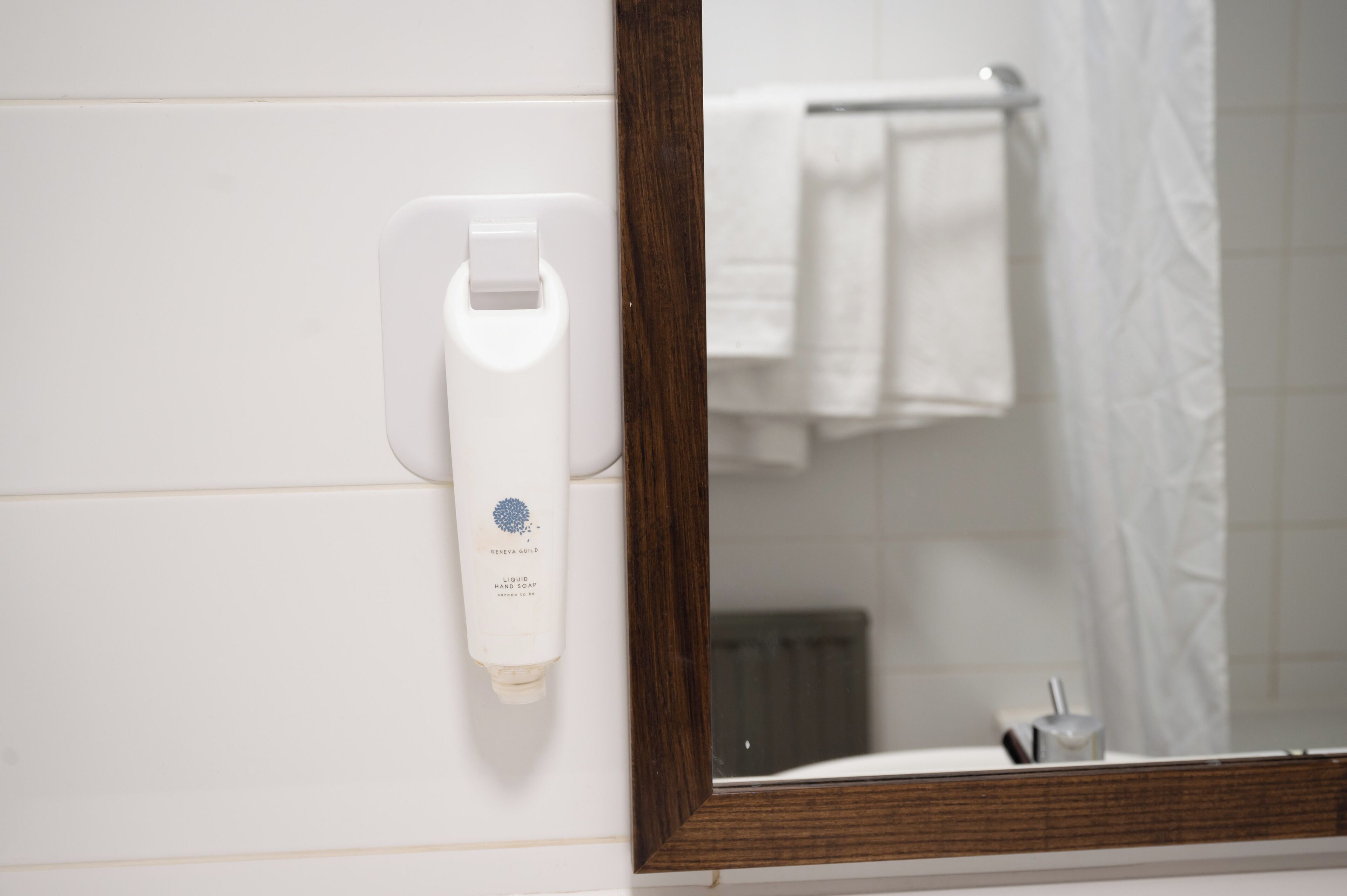 Een badkamer met een witte handdoekhouder, een spiegel en een witte fles vloeibare zeep.