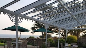 An outdoor patio area with round wooden tables and chairs, covered by a white pergola with green umbrellas. - The Manor Hotel (Dorchester)