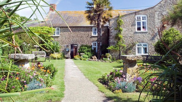 A stone building with a central entrance, surrounded by a garden with various plants and flowers. - The Manor Hotel (Dorchester)