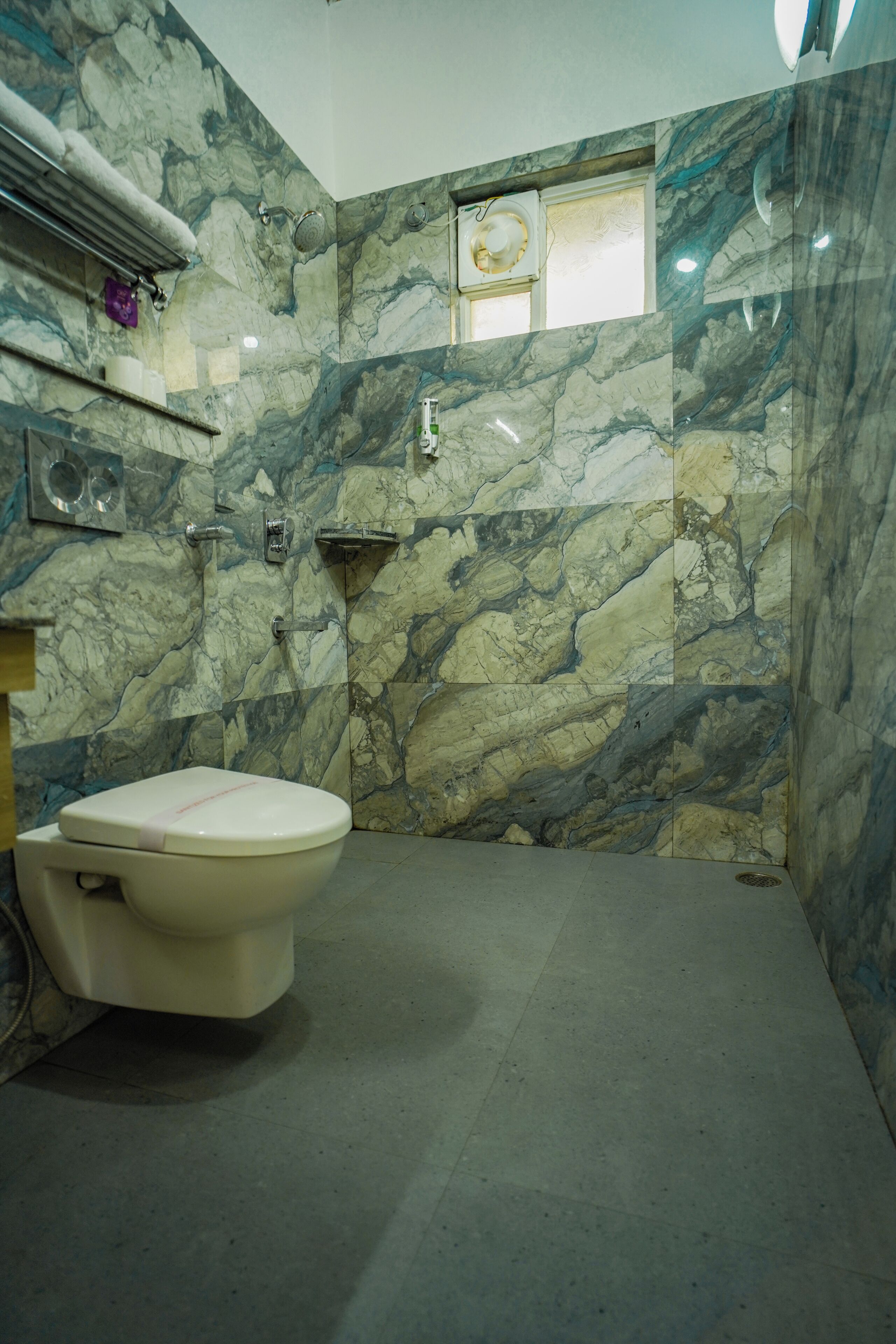 A bathroom with a toilet, marble walls, and a shower area.