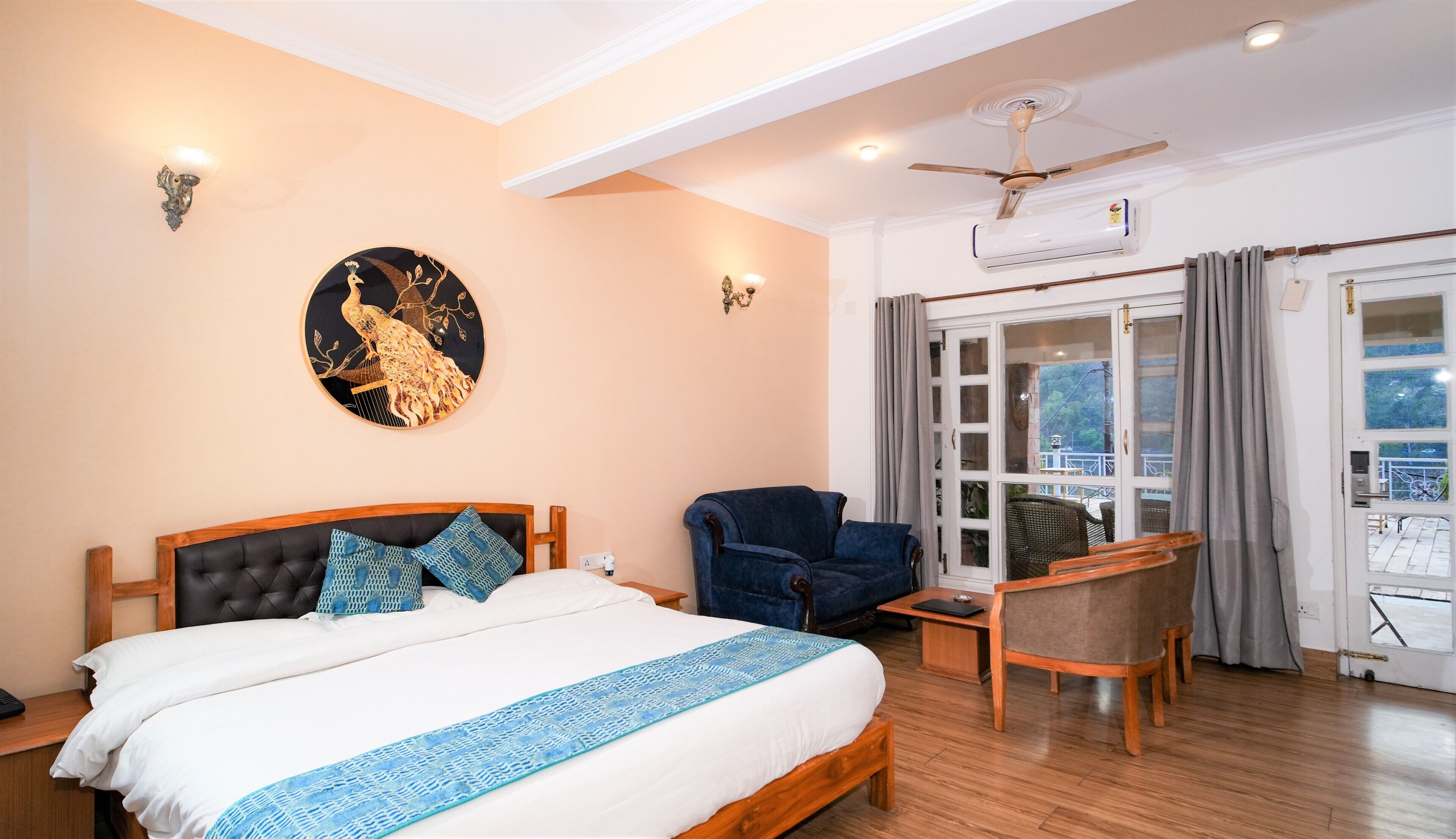 Une chambre d’hôtel avec un lit, une chaise, un bureau, un ventilateur de plafond et une vue sur l’extérieur, visible à travers une porte vitrée.