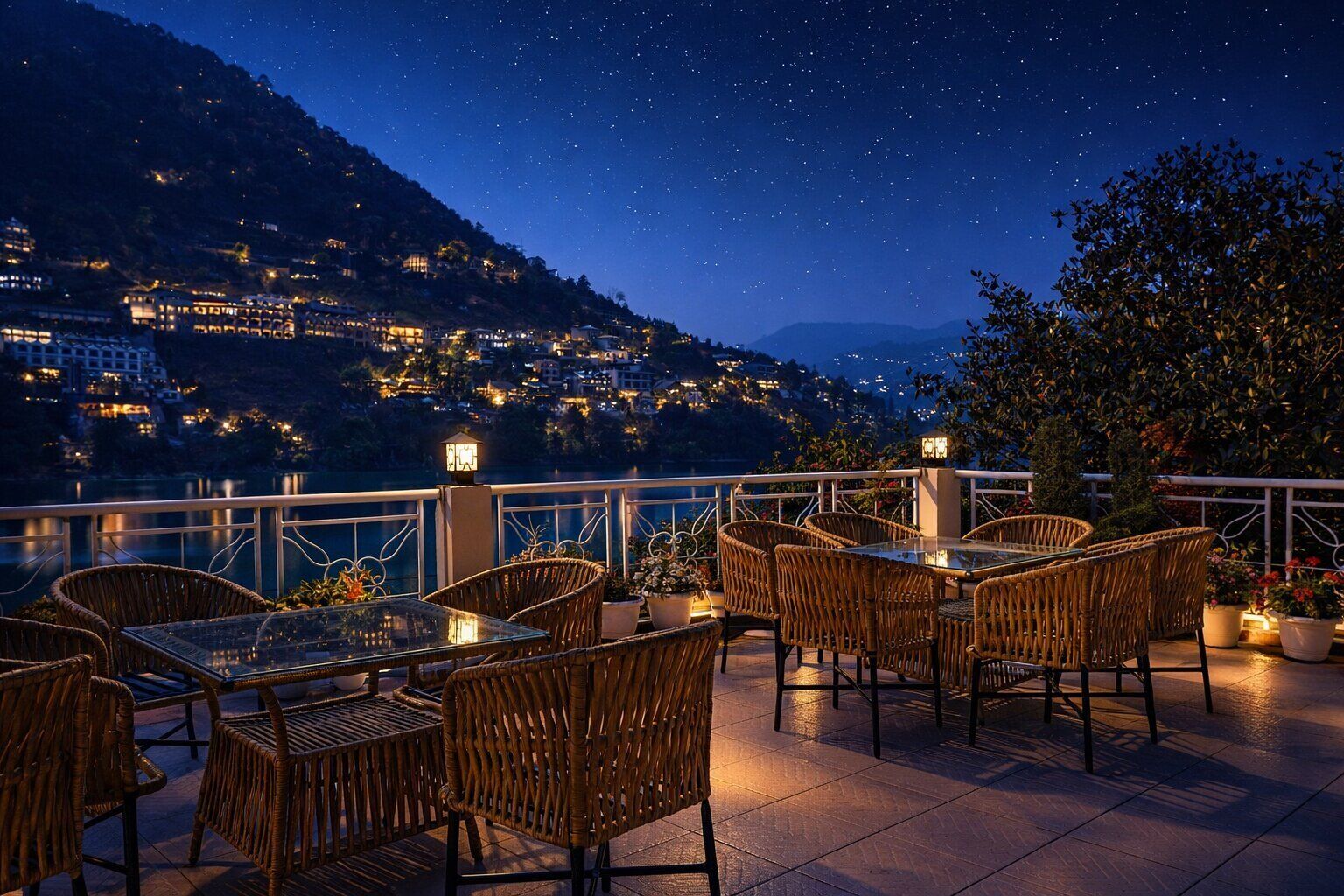A terrace with wicker furniture and potted plants, overlooking a cityscape at night.